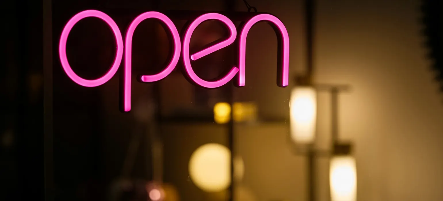 A neon sign that reads open in front of a mirror
