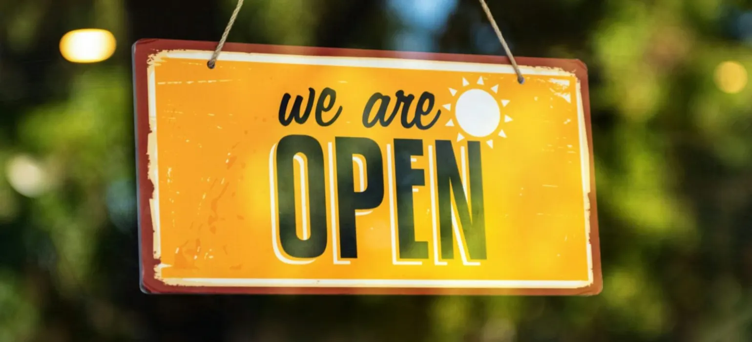 A yellow sign that says we are open hanging from a string